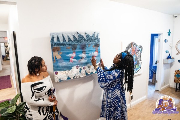 Two women in the museum gallery looking at a textile artwork of midwives and water
