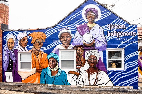 A mural of nine African and Black diasporic midwives across the exterior wall of the African Indigenous Midwifery Museum